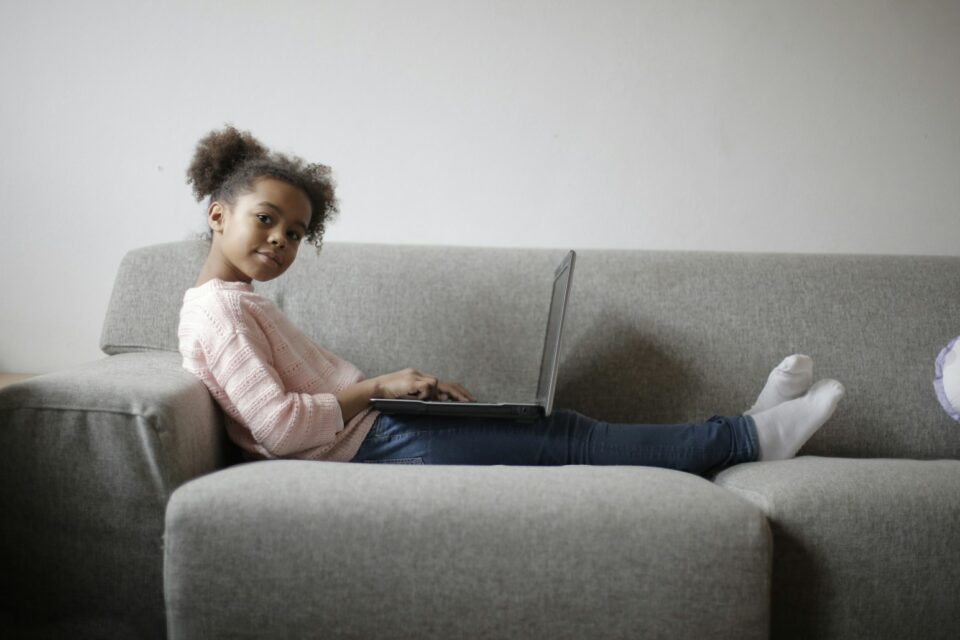 girl in pink long sleeve shirt and black pants sitting on gray couch